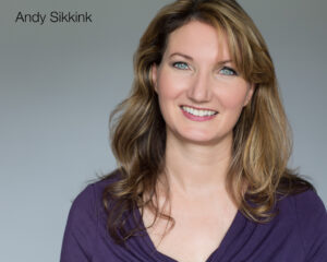 A brown haired woman in a purple shirt with a grey background