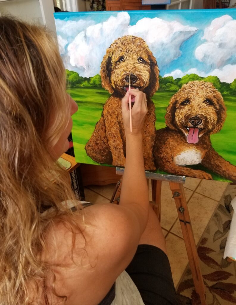 a photo of the artist painting a custom pet portrait of two Golden Doodles named Huck and Finn.